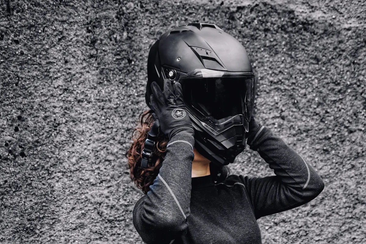 Rider in black gloves and riding top fastening a full-face motorcycle helmet